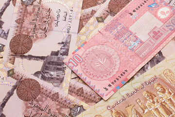 A close up image of a red, ten taka bank note from Bangladesh on a bed of Egyptian one pound bank notes in macro