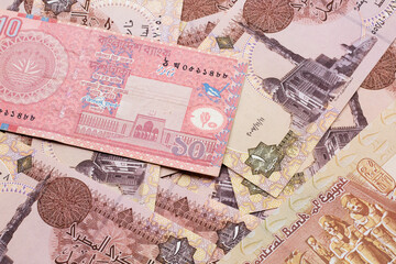 A close up image of a red, ten taka bank note from Bangladesh on a bed of Egyptian one pound bank notes in macro