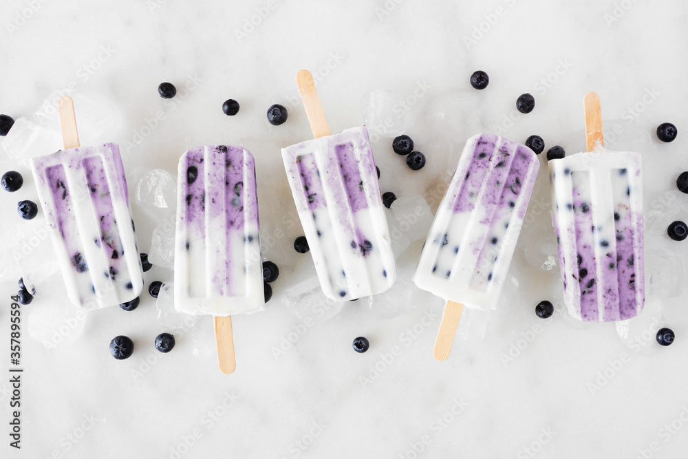 Poster group of blueberry vanilla yogurt ice pops. above view in a row on a white marble background.