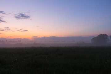 Fototapeta na wymiar Purple sunset over the field and dense fog over the grass
