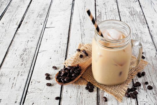 Cold summer iced coffee in a mason jar against a rustic white wood background