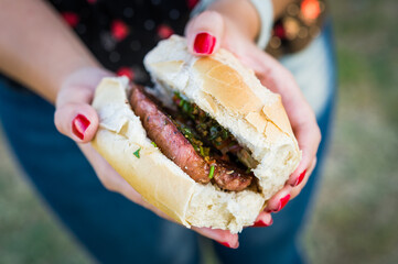 Young woman eating traditional Argentine choripan sandwich at a street food market