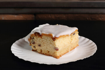 Cheesecake on disposable paper plate. Cheesecake with raisins topped with sugar icing.