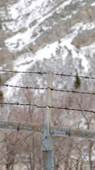 Vertical crop Focus on security chain link fence with barbed wires against on snowy hill slope