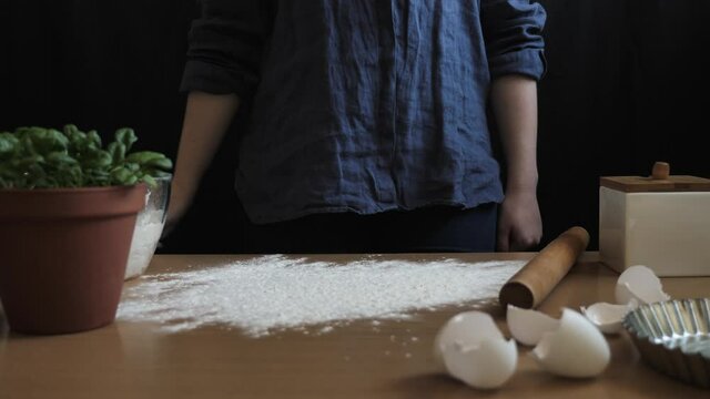 A female housewife or pastry baker kneads the dough on the kitchen table to bake bread or prepare to leave. Lonely girl preparing food. Video taken close-up with natural light in 4k from a tripod