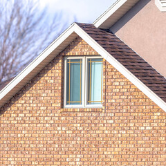 Square Close up of a home exterior with sunlit pitched roof over window and brick wall
