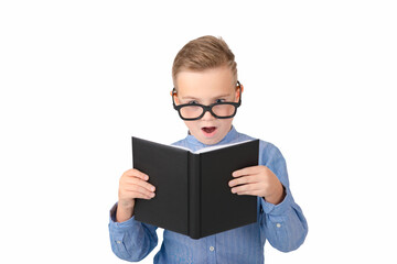 Fototapeta premium Cute dreamy schoolboy reads book and wearing glasses while standing in the studio, isolated over white
