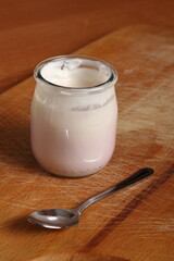 Yogurt in open small glass jar with spoon on wooden cutting boar
