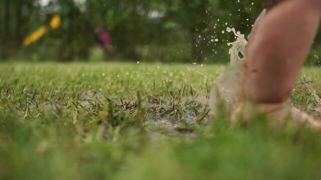 A kid having loads of fun jumping in mud puddle. Clouse up portrait of toddlers bare feet, a child jumping in the grass through a puddle, a happy childhood, have fun