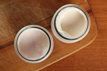 Yogurt in open small glass jar on wooden cutting board. Directly Above.