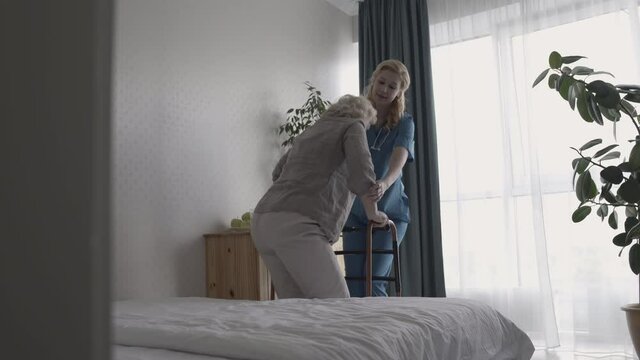 Kind young nurse helping disabled senior lady use walking frame, rehabilitation