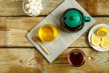 A cup of freshly brewed tea on a table a lemon, honey and sugar.