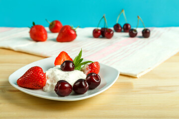 Ice cream dessert with strawberries and cherries in a plate on a wooden table next to the scattered berries.