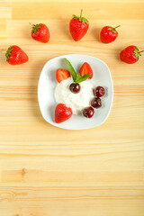 Ice cream dessert with strawberries and cherries in a plate on a wooden table. Copy space.