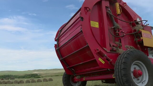 the baler collects the grass in a roll in the field. closeup. in rural areas