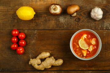 Traditional thai tom yam soup with chicken in a cup with spoon and vegetables nearby.