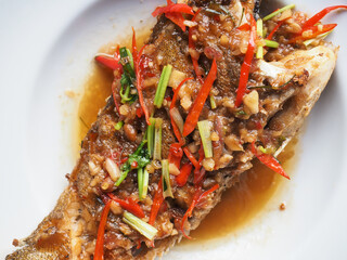 Top view fried fish in sweet and sour sauce with chili pepper and spring onion