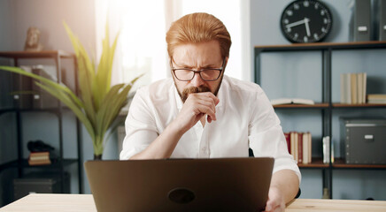 Front view of attentive mature businessman in white shirt and glasses working on computer in office