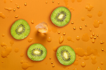 Fresh juicy slices of kiwi fruit on bright orange background covered with water drops. Creative...