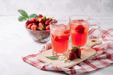 A refreshing summer drink made from strawberries, juice, soda with ice cubes and slices of berries, in a beautiful glass with water droplets, still life of cocktails on a wooden board, red napkin