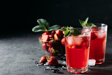 A refreshing summer drink made from strawberries and mint, juice, soda with ice cubes and berry slices, in a beautiful glass with water droplets on a wooden board, dark background with place for text
