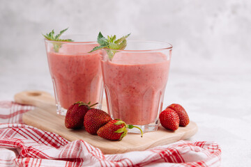 Strawberry smoothie with mint in glasses on a wooden board with a beautiful serving of red napkin on a light background. Still life with place for text.