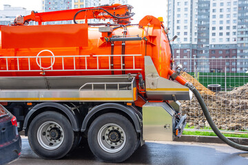 Pumping water from sewage canals during the construction of roads in the city. Truck with orange water tank.