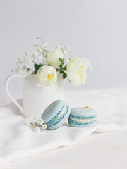 Tasty blue  french macarons and jar with cream roses on a white wooden background.