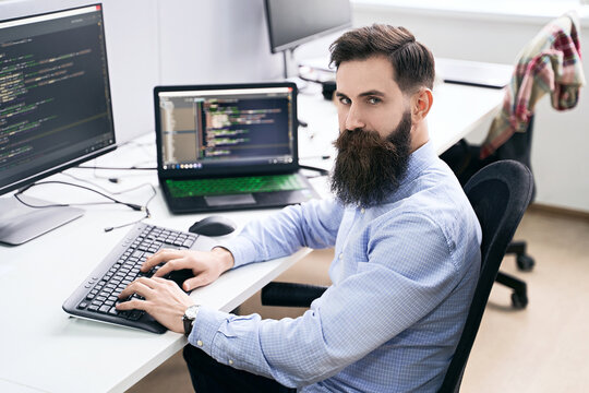 Serious computer programmer developer working in IT office, sitting at desk and coding, working on a project in software development company or startup. High quality image.