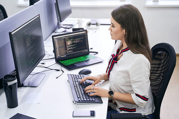 Beautiful female junior software developer working on computer in IT office, sitting at desk and...