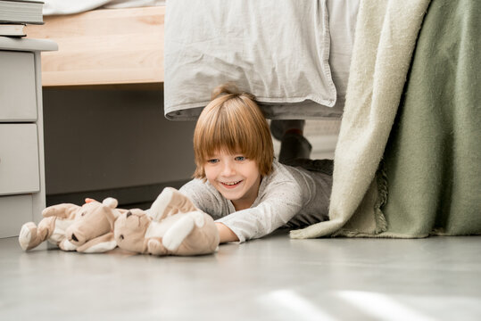 the boy is playing on the floor, crawled out from under the bed. hid. Cozy bright bedroom. Active games. lies and laughs
