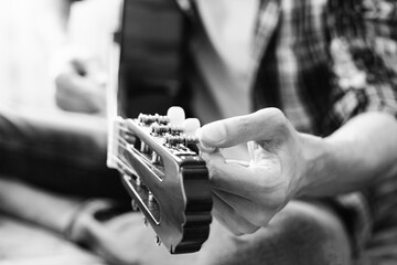 Male hands tuning guitar strings. Black and white concept. Close-up.