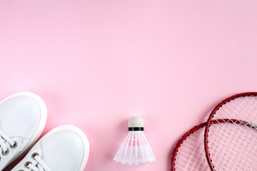 Sport flat lay with shuttlecock, two rackets for playing badminton and white sneakers on a pink background. Concept healthy lifestyle. Top view. Copy space.