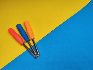 Three screwdrivers of different colors vertically on a yellow and blue background with a copy of the space.
