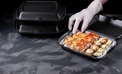 Cook wearing disposable gloves is packing sushi rolls into the black container. Food delivery...