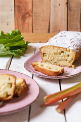 geschnittener, frischer Kuchen mit Rhabarber, Puderzucker und Eierlikör auf einem Tisch aus Holz in der Küche am Nachmittag