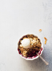 Crumble with berries, apples, ball of ice cream almond in white bowl close up