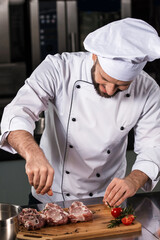 Man chef cooking steak at kitchen restaurant. Chef in uniform salt meat.