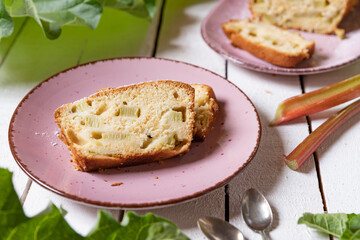 geschnittener, frischer Kuchen mit Rhabarber, Puderzucker und Eierlikör auf einem Tisch aus Holz in der Küche am Nachmittag