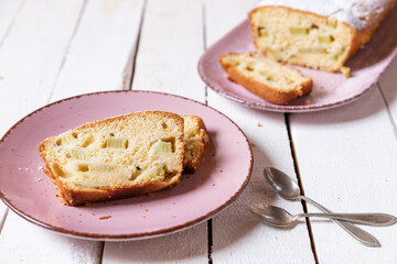 geschnittener, frischer Kuchen mit Rhabarber, Puderzucker und Eierlikör auf einem Tisch aus Holz in der Küche am Nachmittag