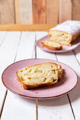 geschnittener, frischer Kuchen mit Rhabarber, Puderzucker und Eierlikör auf einem Tisch aus Holz in der Küche am Nachmittag