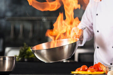 Chef hands hold wok with fire. Closeup chef hands prepare food with fire.