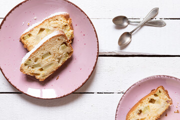 geschnittener, frischer Kuchen mit Rhabarber, Puderzucker und Eierlikör auf einem Tisch aus Holz in der Küche am Nachmittag