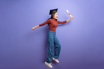 Portrait of young University student woman with graduation cap on violet background
