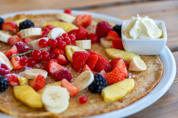 Large pancake with fresh summer fruit and whipped cream on a wooden table. Close up.