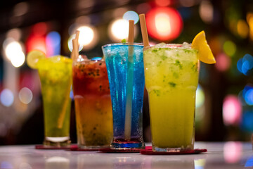 Fresh multicolour beverages in a fine dine restaurant garnished with lemon piece and ecofriendly wooden straw with bokeh background