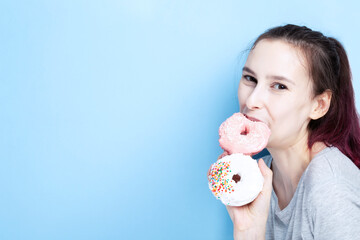 Young girl holds two donuts in her hand and bites one, blue background