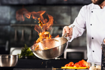 Chef hands keep wok with fire. Closeup chef hands cook food with fire. - obrazy, fototapety, plakaty