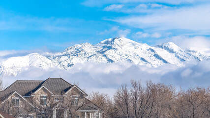 Panorama frame Peaks of a magnificent snowy mountain over low puffy clouds against blue sky