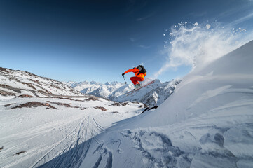 Athlete male skier jumps from a snow-covered slope against the backdrop of a mountain landscape of snow-covered mountains on a sunny day. The concept of winter sports wide angle